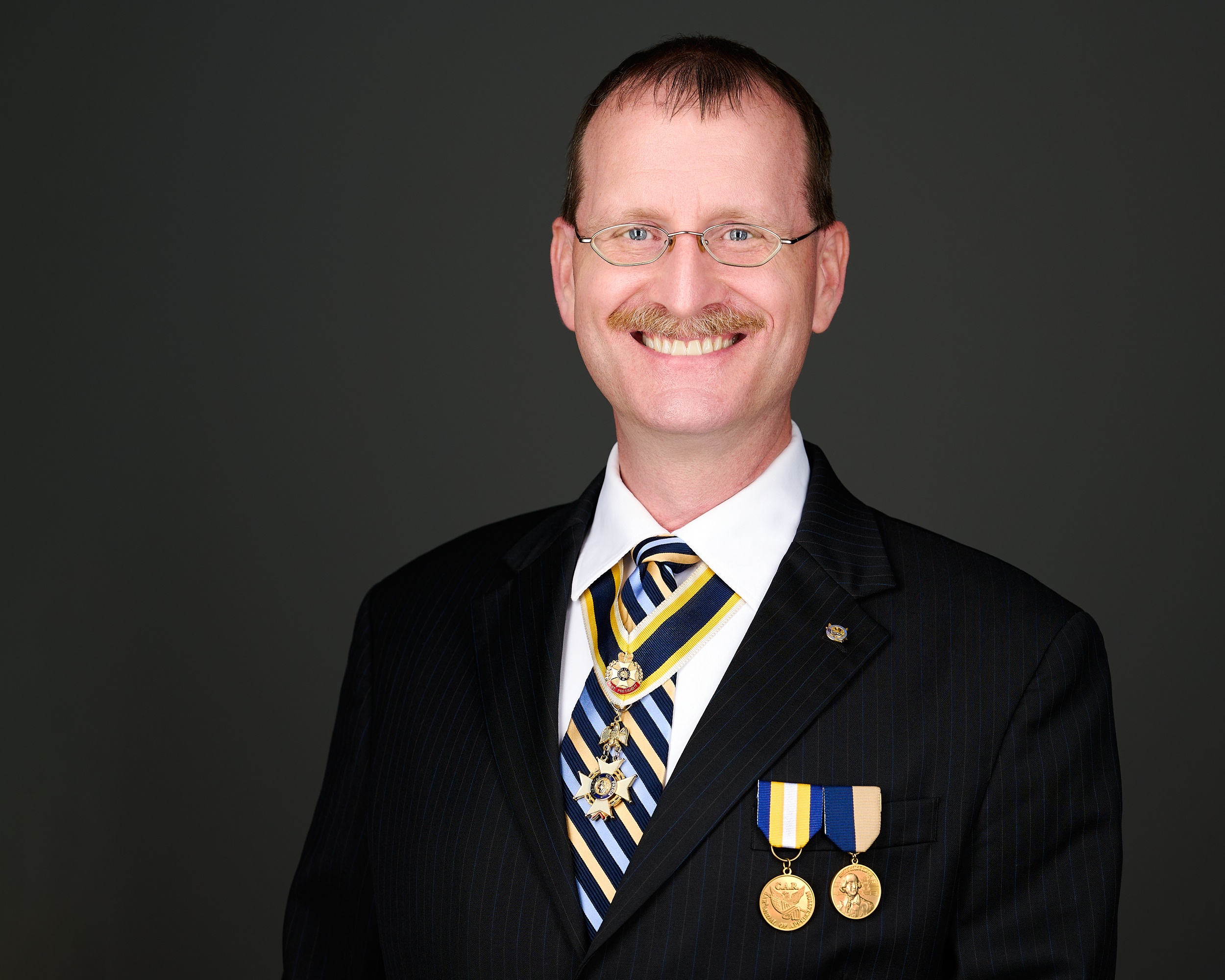 Virginia SAR President Darrin Schmidt, in dark business suit with SAR medals